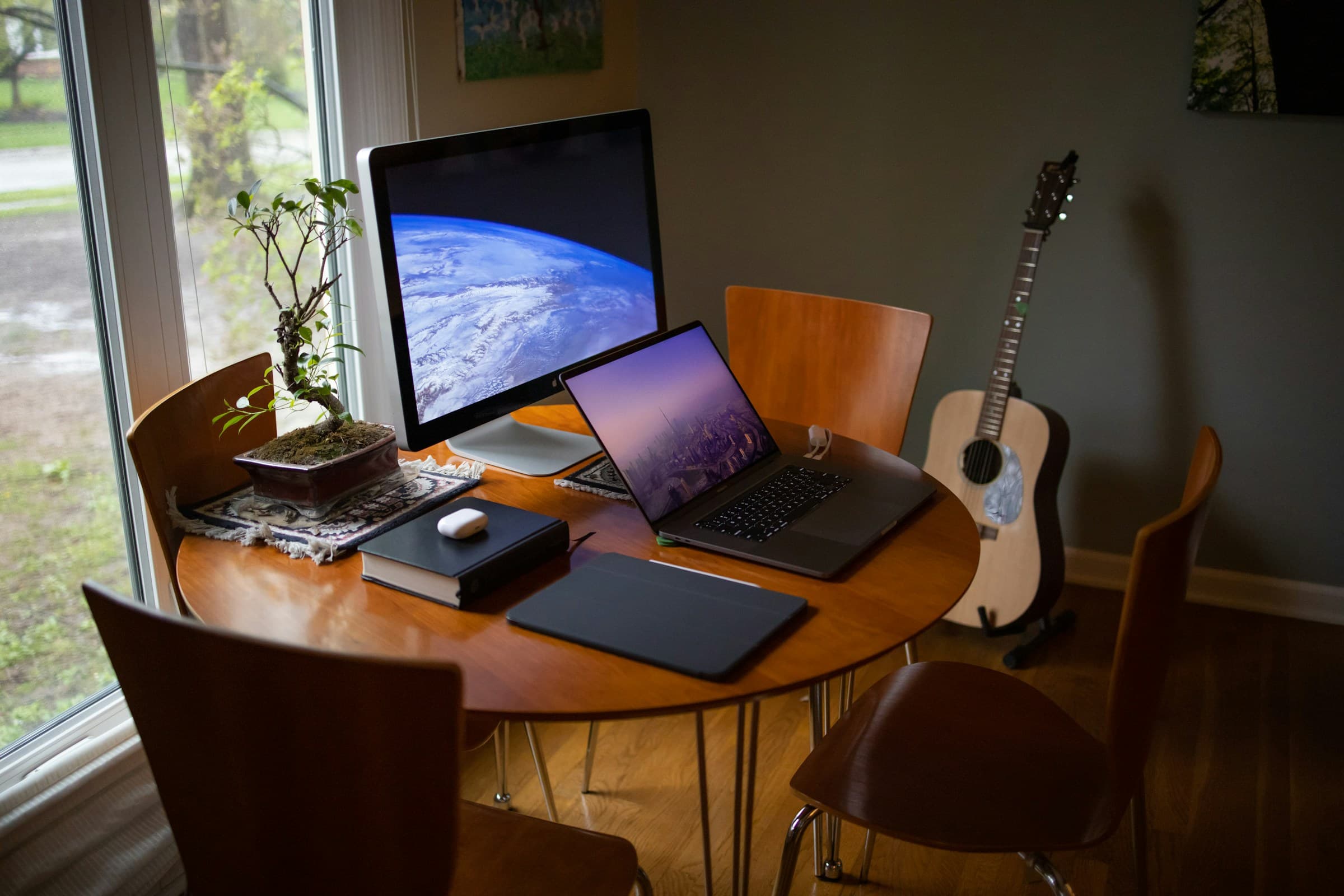 Table ronde près d’une fenêtre utilisée comme bureau, avec ordinateur portable, écran et chaises dans un salon