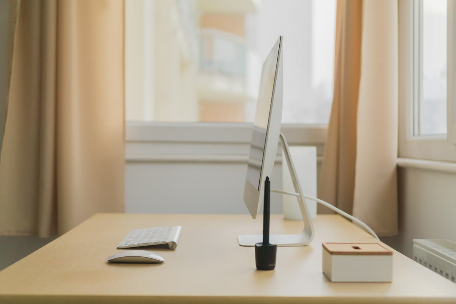 Bureau en bois clair près d'une fenêtre, lumière douce, clavier et souris, un seul câble discret