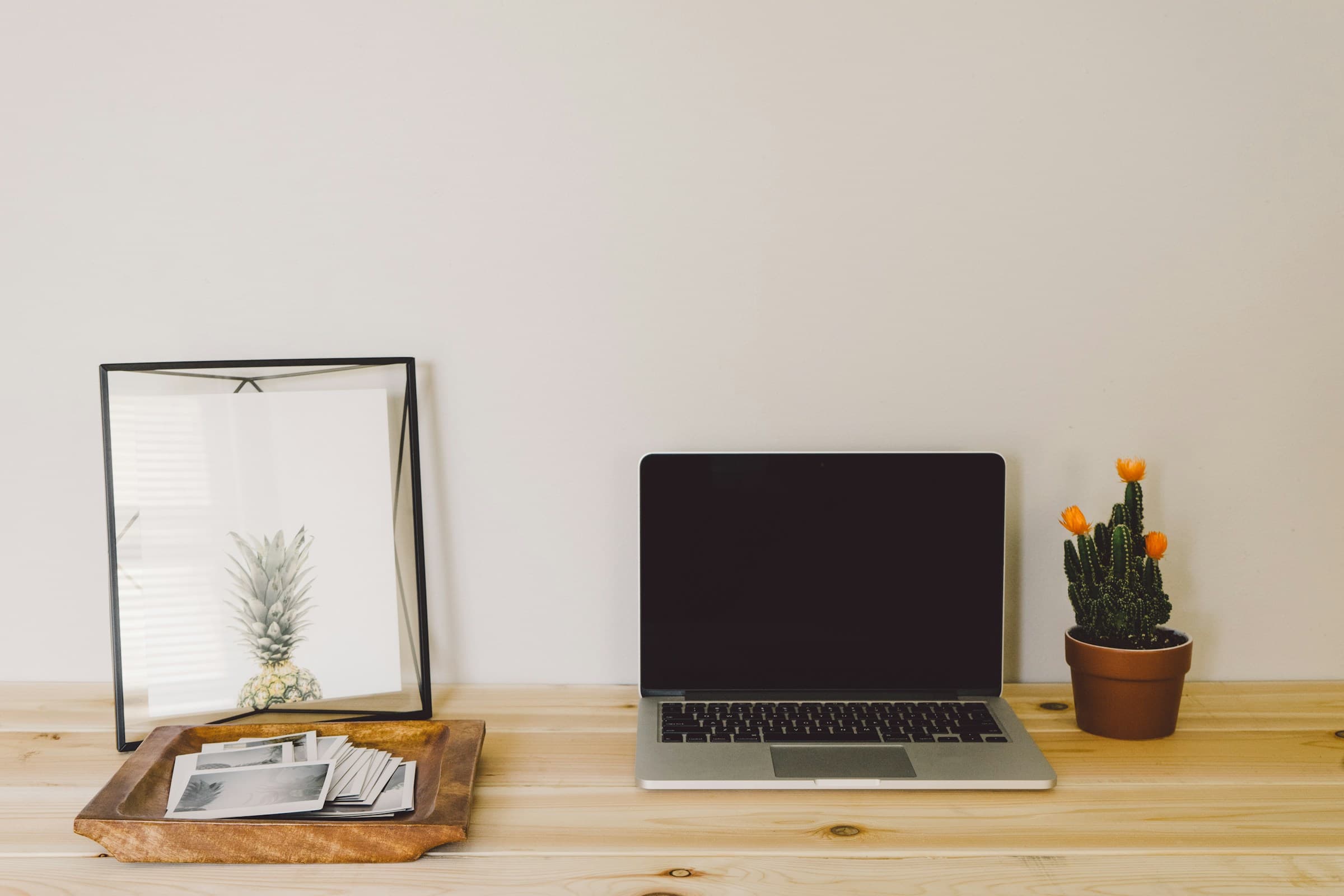 Light wood desk with an open laptop, shallow document tray, and cactus