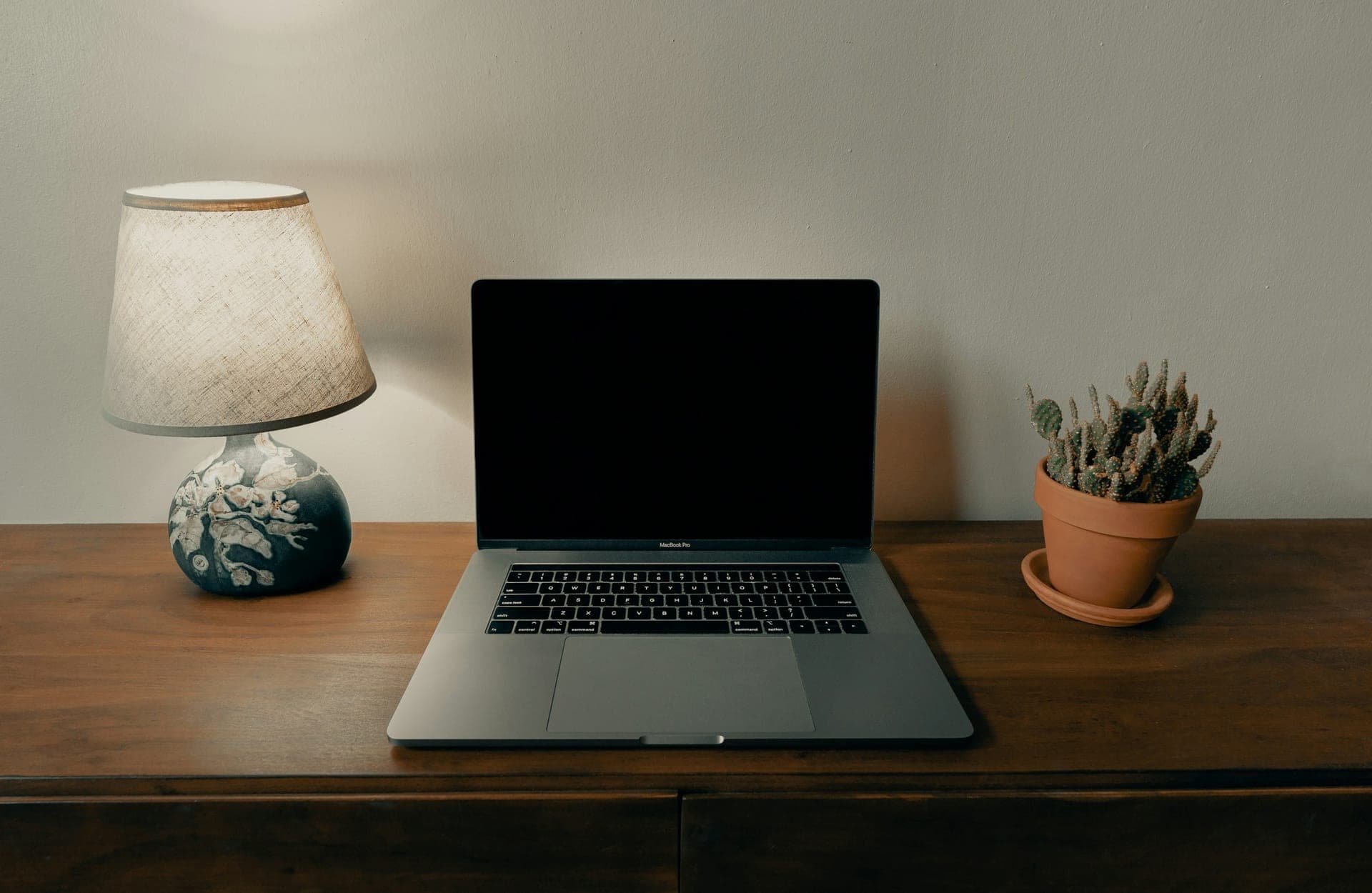 Ordinateur portable ouvert sur un bureau en bois, entre une lampe et un cactus